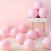 A set of pink and purple balloons displayed on a white wooden stand against a light pink background.