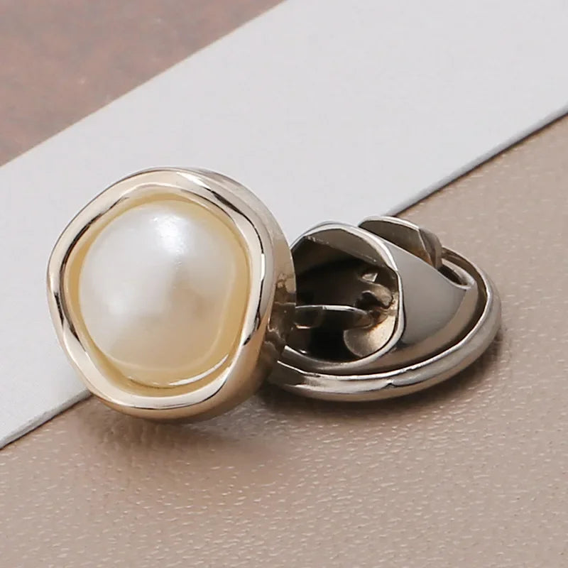A pair of gold-toned pearl and rhinestone no-sew brooch buttons resting on a light surface.