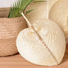 A light beige peach-shaped bamboo woven hand fan resting in a natural woven basket.