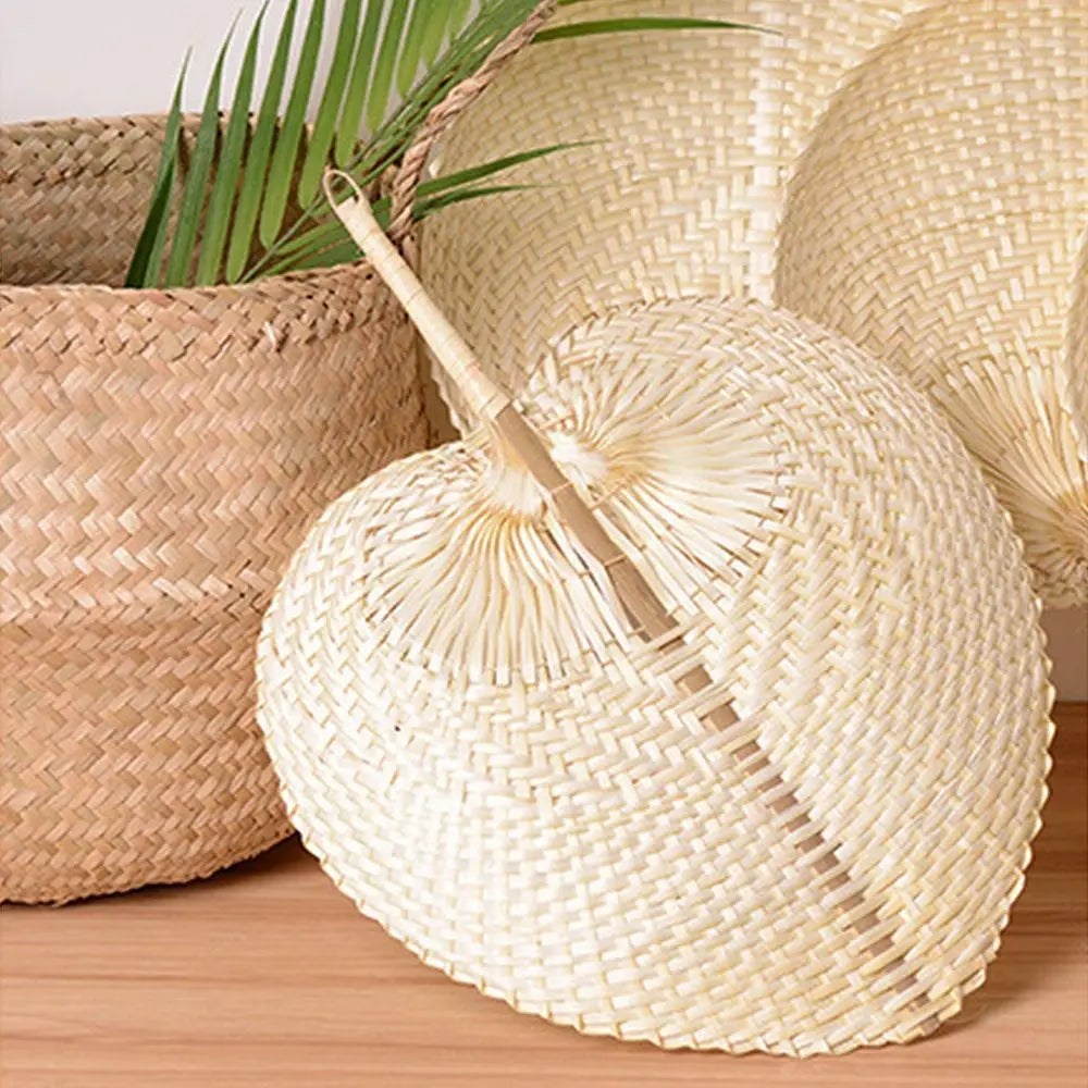 A light beige peach-shaped bamboo woven hand fan resting in a natural woven basket.