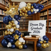 A balloon arch kit featuring navy blue, white, and gold balloons arranged in a crown shape.