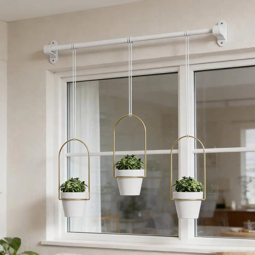 Ein Set aus drei goldfarbenen Hängepflanztopfhalter, aufgehängt an einem weißen Fensterstab.