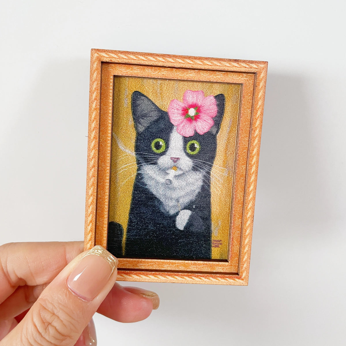 Retrato de acuarela enmarcado de un gato blanco y negro con ojos verdes y flores rosas.