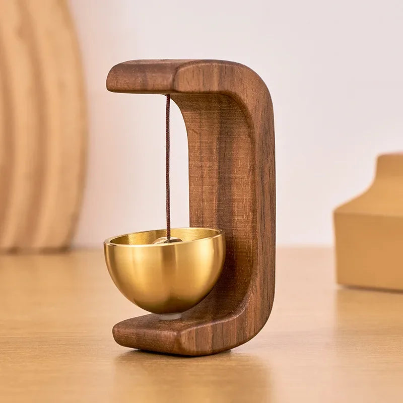 A wooden doorbell with a copper bell suspended by a string, resting on a wooden surface.