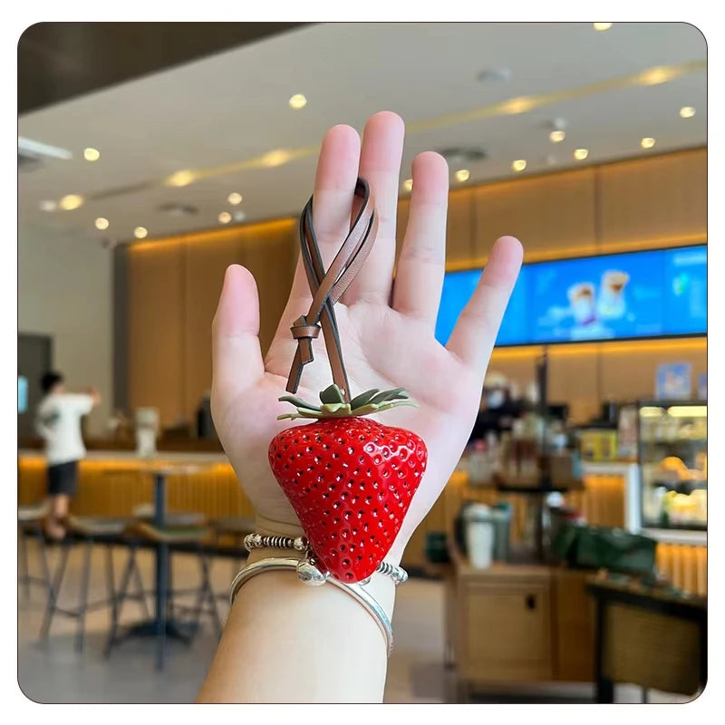 A hand holds a red strawberry charm and keychain in a modern cafe setting.