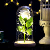 An eternal rose LED light simulation flower displayed in a glass enclosure on a dark surface.