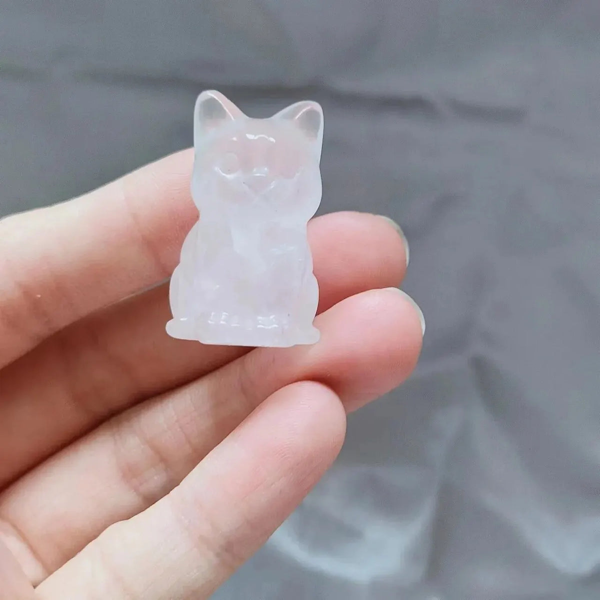 Un ornement de chat en cristal clair sculpté à la main est tenu dans la main d'une personne sur un fond gris.