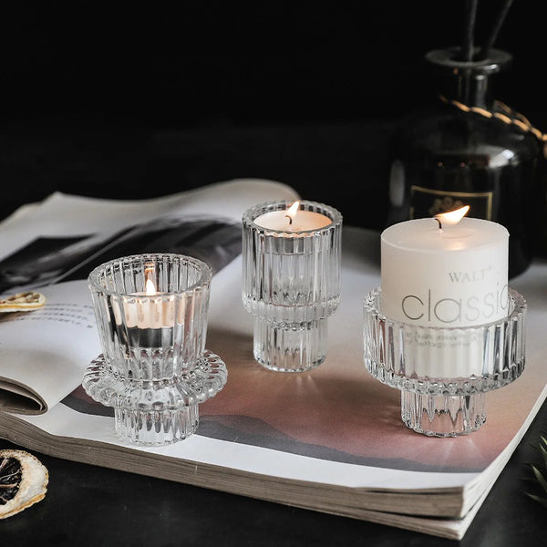 Clear glass pillar tealight candle holders displayed on a book with a dark background.