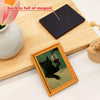 A framed fridge magnet featuring a black cat drinking from a glass of red wine, set on a wooden board.