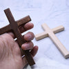A hand holds a dark brown wooden wall cross and a light beige wooden wall cross on a white marble surface.