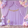 A purple draped backdrop for a birthday party featuring balloons and a cake.