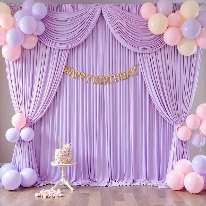 A purple draped backdrop for a birthday party featuring balloons and a cake.