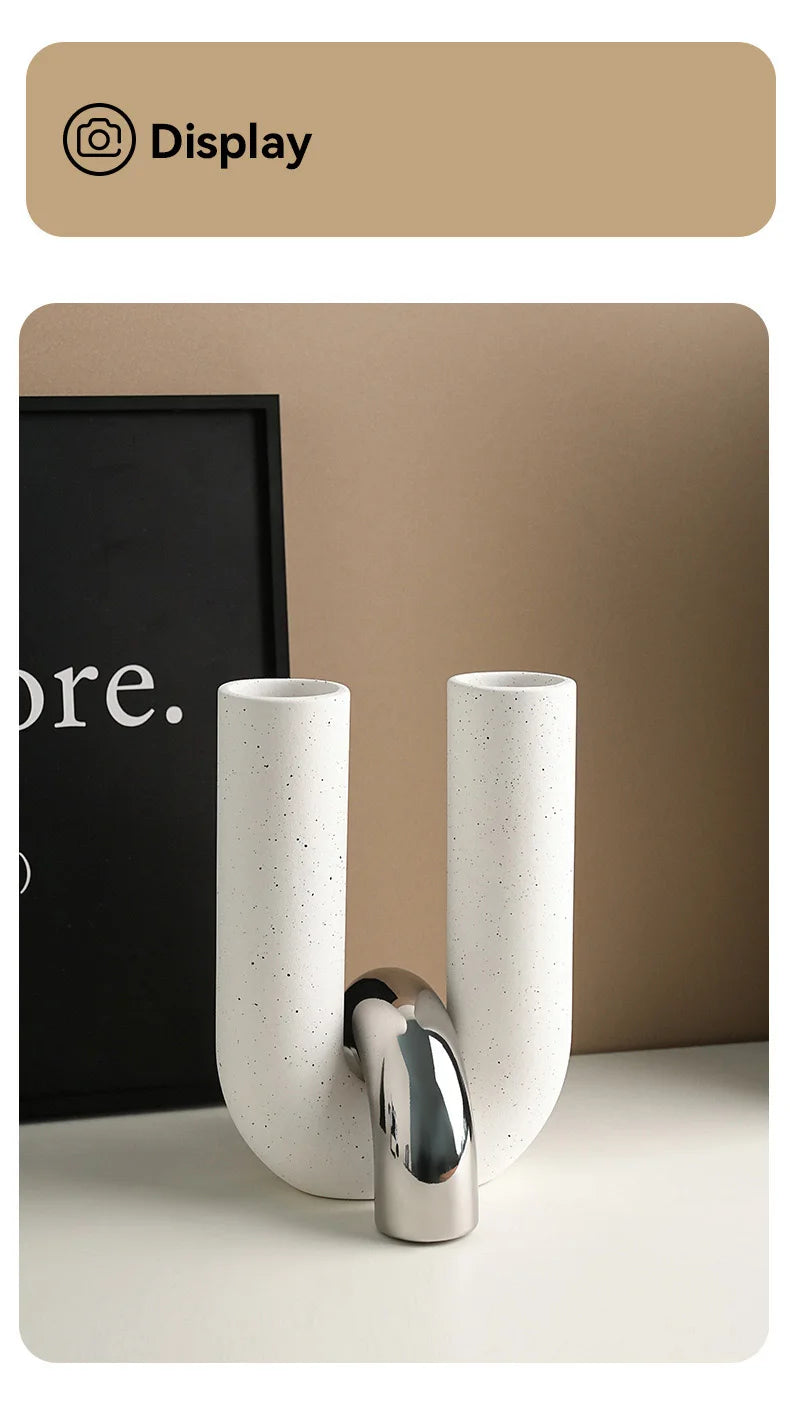 A white ceramic U-shaped tabletop vase with a chrome finish is displayed on a light surface.