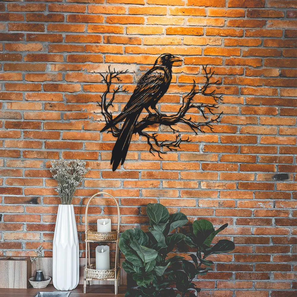 Metal wall art depicting a black raven perched on a bare tree branch against a brick background.