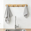A solid beech wood wall hook rack with four hooks mounted above a stainless steel kitchen sink.