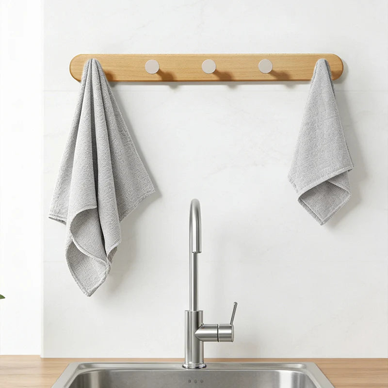 A solid beech wood wall hook rack with four hooks mounted above a stainless steel kitchen sink.