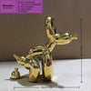 A shiny gold balloon dog sculpture in a squatting pose displayed on a white surface.