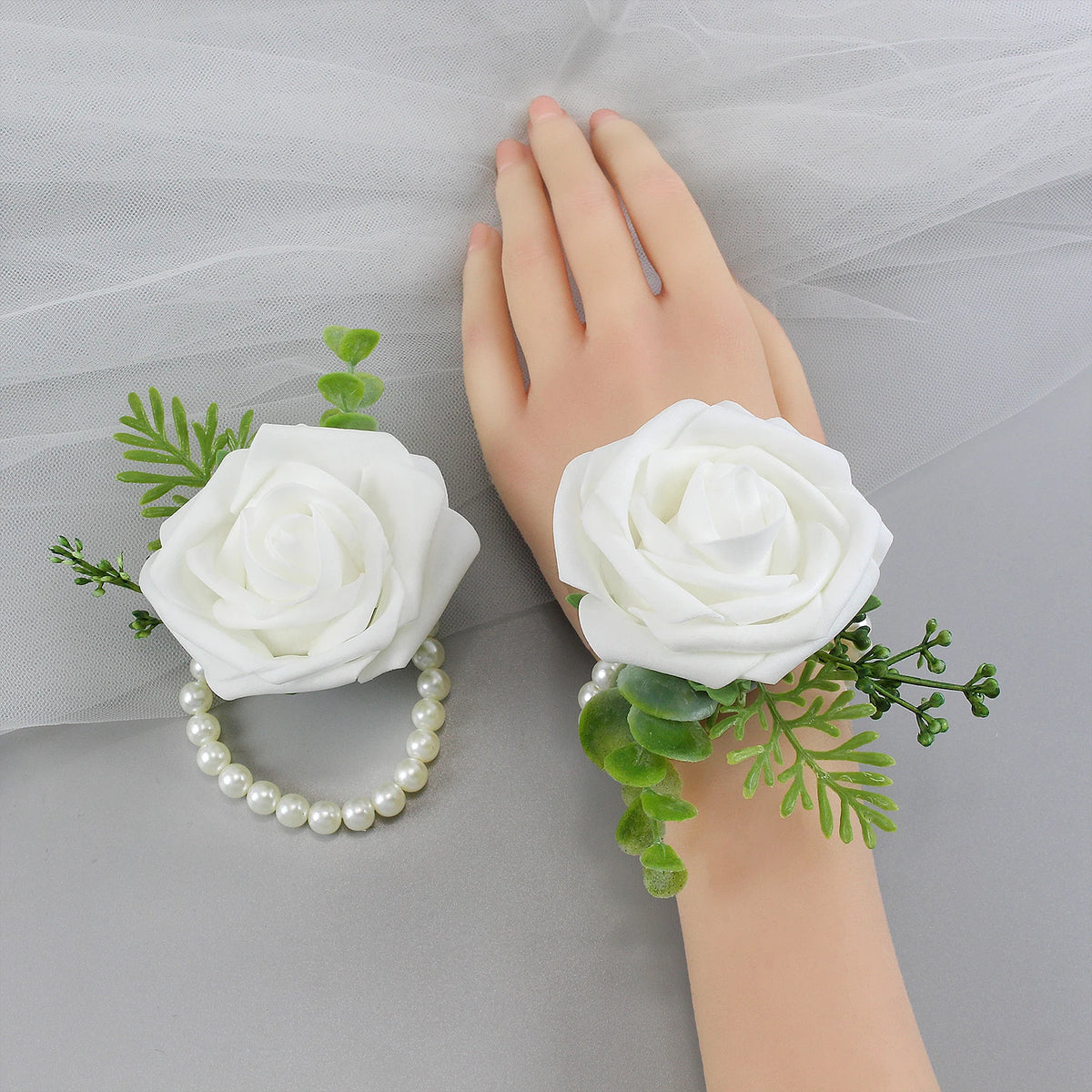 A hand is holding a white rose corsage bracelet with green foliage for a wedding.
