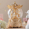 Adorno de caja de música con bola de cristal dorada y blanca y detalles intrincados sobre una base decorativa.