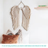 Handwoven angel wing macrame wall hanging made of natural beige fibers displayed on a white wall.