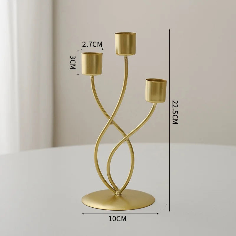 A gold-colored iron candle holder with three slender arms and a round base, shown against a light background.