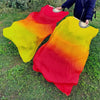 A vibrant silk ribbon dance fan with a gradient of yellow, orange, and red is being held outdoors.