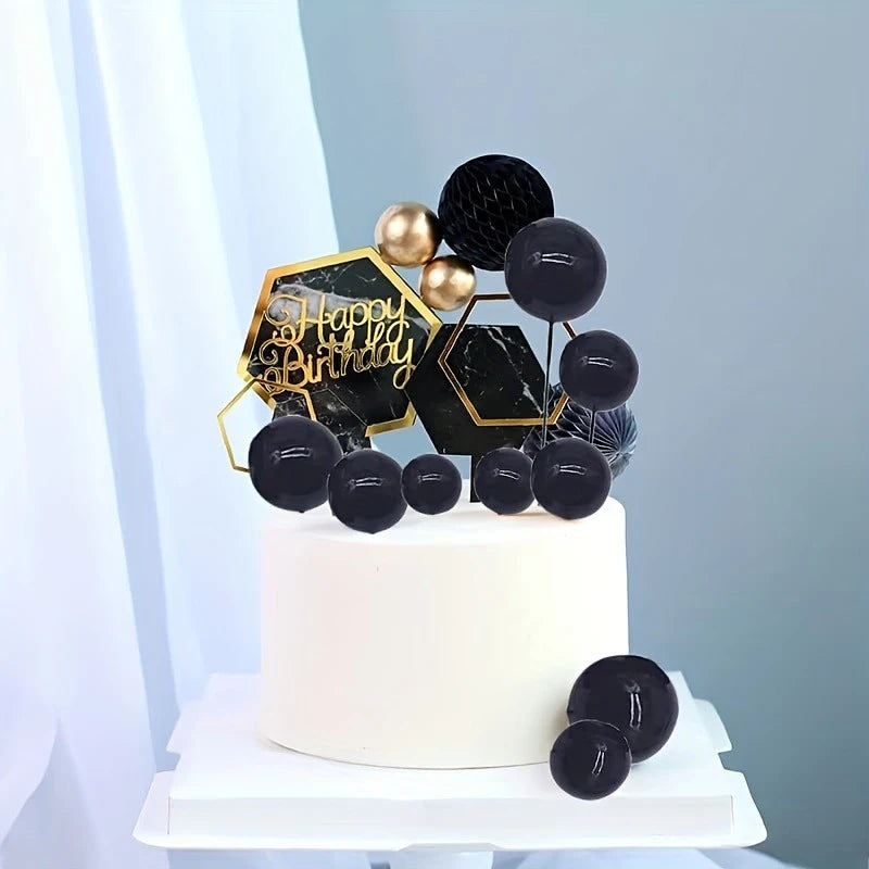 A white cake decorated with gold and black foam ball toppers for a birthday party display.