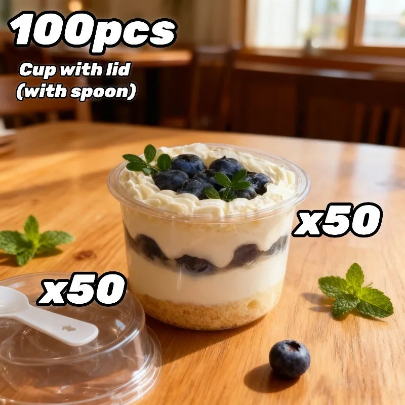 A clear plastic cup filled with a layered dessert featuring blueberries and cream, shown next to a spoon and mint leaves.
