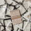 A beige lace sticker book with a decorative cover lies on a white background surrounded by black and white lace fabric.