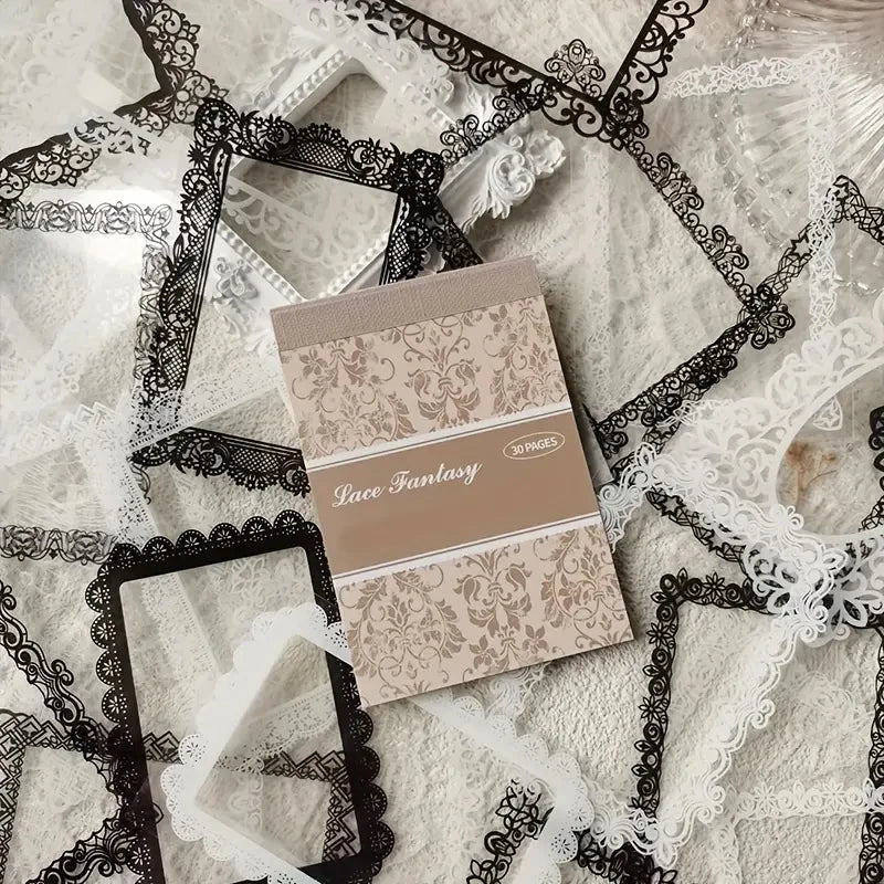 A beige lace sticker book with a decorative cover lies on a white background surrounded by black and white lace fabric.