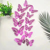 A set of twelve pink and purple 3D butterfly wall stickers displayed on a white surface next to a potted green plant.