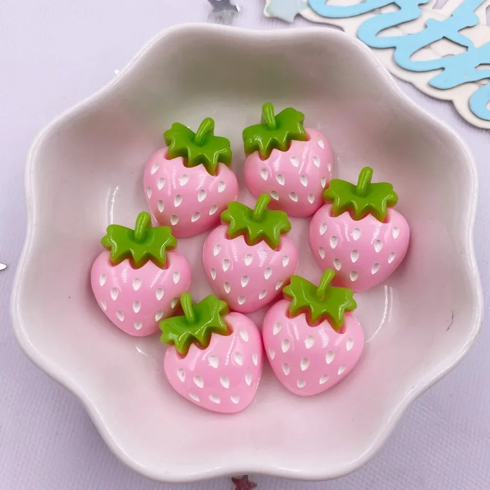 Pink strawberry resin flatback charms with green leaves arranged in a white dish.