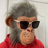 A realistic chimpanzee latex mask with gray fur and brown skin wearing sunglasses and a red hoodie.