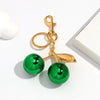 Gold-toned pendant keychain featuring a green resin cherry charm on a white background.