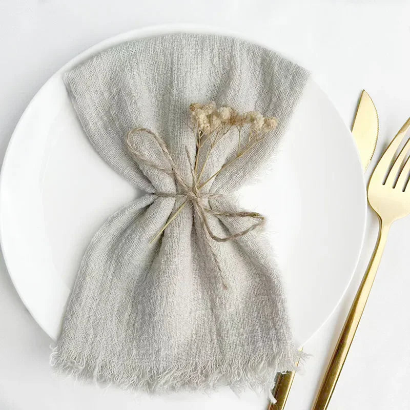 A gray handcrafted cotton napkin bundle tied with twine placed on a white plate next to a gold fork.