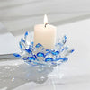 A clear crystal lotus candle holder with a white pillar candle and a lit wick on a white surface.