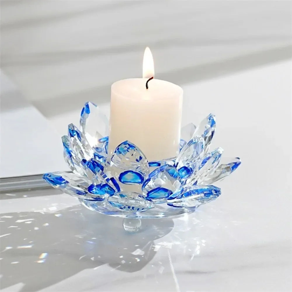 A clear crystal lotus candle holder with a white pillar candle and a lit wick on a white surface.