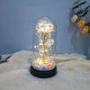 Una cloche de vidrio que contiene una rosa dorada brillante con delicadas partículas de luz interna