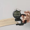A hand holds a digital measuring tool used for applying wood grain peel-and-stick floor and wall stickers onto a wooden surfa