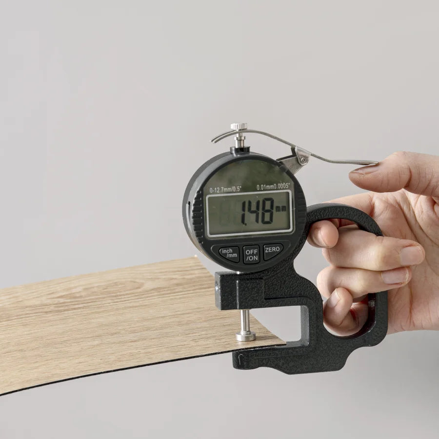A hand holds a digital measuring tool used for applying wood grain peel-and-stick floor and wall stickers onto a wooden surfa