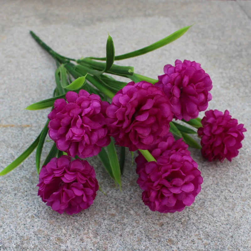 Un bouquet de fleurs d'hydrangea artificielles violettes avec des tiges vertes sur une surface grise.