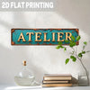 A vintage industrial metal wall sign with the word ATELIER in distressed turquoise and golden lettering mounted on a white wa