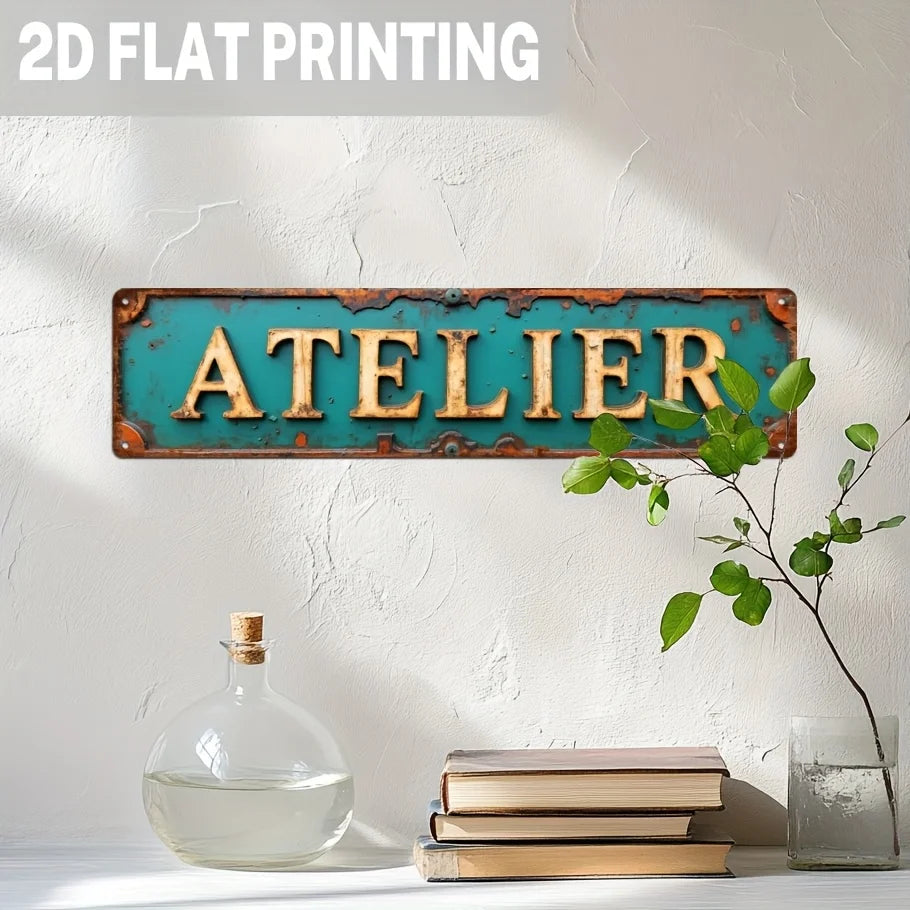 A vintage industrial metal wall sign with the word ATELIER in distressed turquoise and golden lettering mounted on a white wa