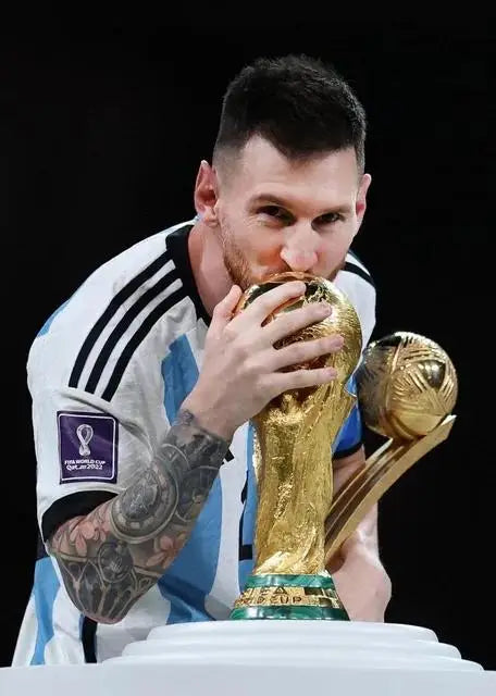 Un hombre con barba y tatuajes sostiene un trofeo de fútbol dorado, celebrando un logro deportivo.