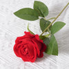 A single vibrant red artificial rose with green leaves on a white textured background.