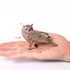 A realistic figurine of an owl resting on a human hand, showing its size.