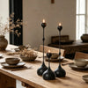A set of three black candle holders with flickering flames resting on a wooden table.