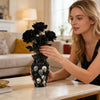 A woman holds a black decorative vase filled with resin skulls in a living room setting.