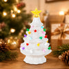 A white ceramic Christmas tree decorated with multicolor LED lights, set against a blurred holiday background.
