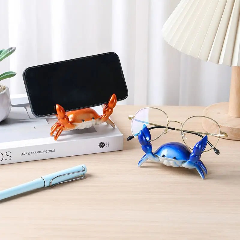 An orange crab-shaped desk organizer holding a pen and a black phone holder on a wooden table.